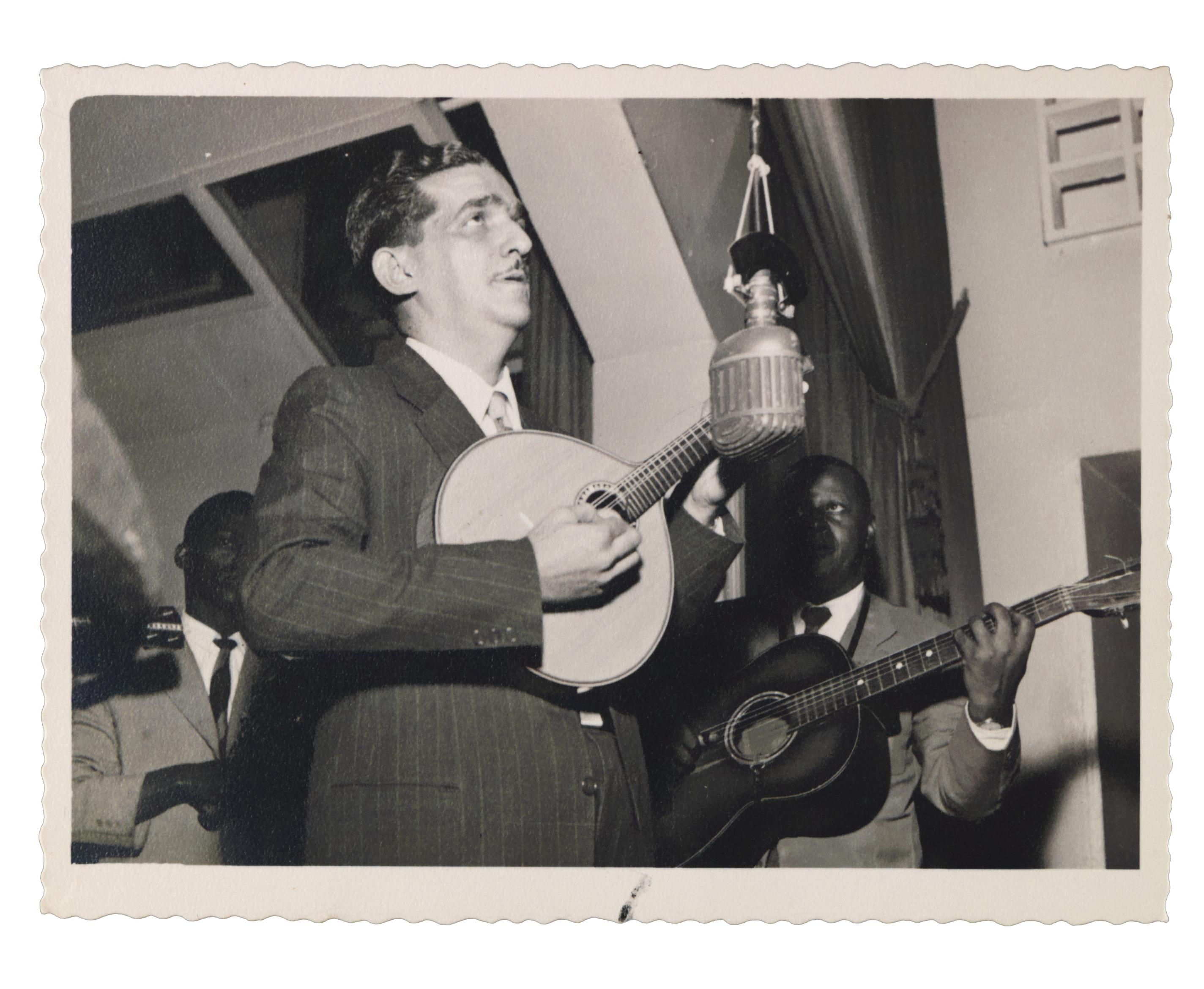 Jacob do Bandolim toca seu instrumento musical em emissora de rádio, próximo ao microfone e homens não identificados, 1930 - 
          Fotógrafo não identificado - 
          Coleção Jacob do Bandolim - 
          Acervo FMIS/RJ